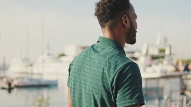 Limanda arka planda yatları olan gülen genç bir adam.