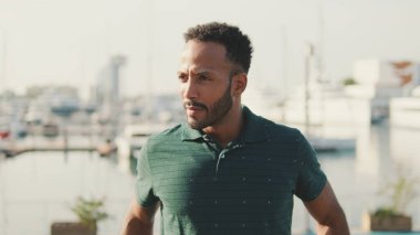 Genç gülen adam limanda arka planda yatlarla oturuyor.