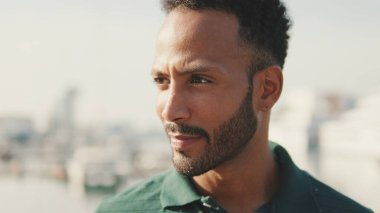 Genç gülen adam limanda arka planda yatlarla oturuyor.