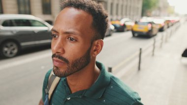 Genç adam sokakta yürür ve etrafa bakar.