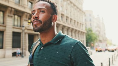 Genç adam sokakta yürür ve etrafa bakar.