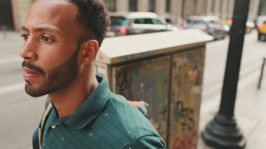 Genç adam sokakta yürür ve etrafa bakar.