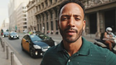Sokakta dikilen mutlu genç adama yakın çekim. Adam kafasını çevirir ve kameraya gülümser.
