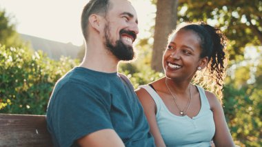 Interracial couple talking while sitting on bench. Backlight