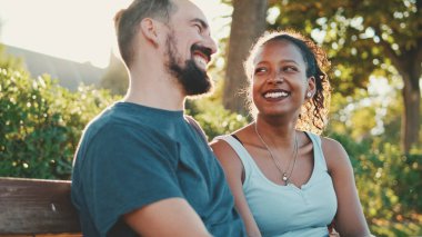 Interracial couple talking while sitting on bench. Backlight