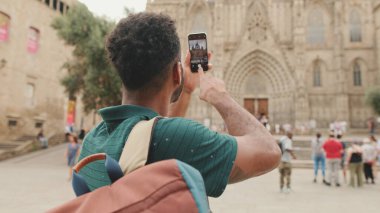 Genç turist, eski şehrin meydanında dururken cep telefonuyla fotoğraf çekiyor. Arka plan