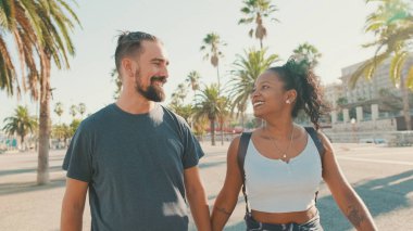 Happy interracial couple walking talking and smiling down the street holding hands