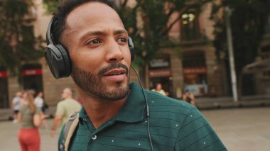 Genç bir turist eski şehrin meydanında yürüyor, kulaklıkla müzik dinliyor..