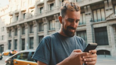 Young man with beard walks down the street using cellphone