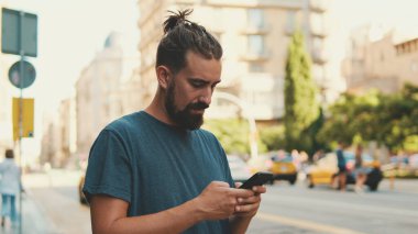 Young man with beard is using cellphone on the background of passing cars