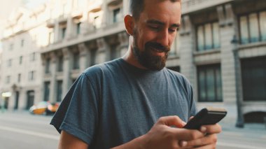 Young man with beard walks down the street using cellphone