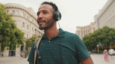 Genç bir turist eski şehrin meydanında yürüyor, kulaklıkla müzik dinliyor.