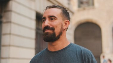Young smiling man with beard walking and looking around at the old city background