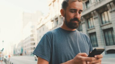 Young man with beard walks down the street using cellphone