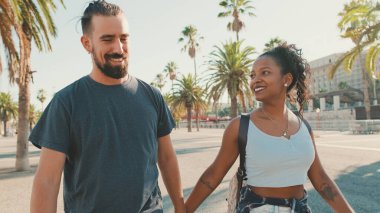 Happy interracial couple walking talking and smiling down the street holding hands