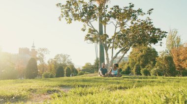 Happy smiling interracial couple talking while sitting on the grass in the park. Backlight