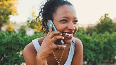 Laughing young mixed race woman sitting on park bench talking on cellphone