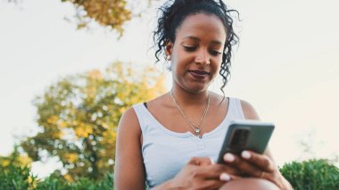Laughing young mixed race woman sitting on park bench using cellphone