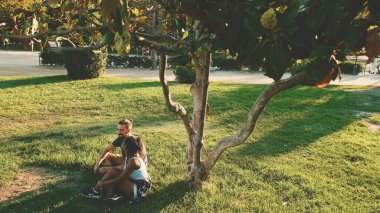 Happy smiling interracial couple talking while sitting on the grass in the park. Backlight