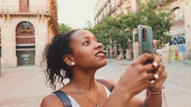 Young mixed race woman uses cell phone, takes photo of the old city