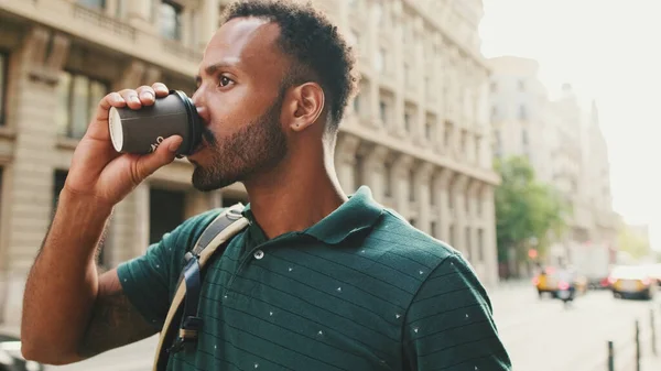 Young man walks down the street, looks around and drinks coffee