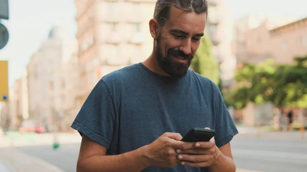 Young Smiling Man Beard Uses Cellphone Walks Street — Zdjęcie stockowe