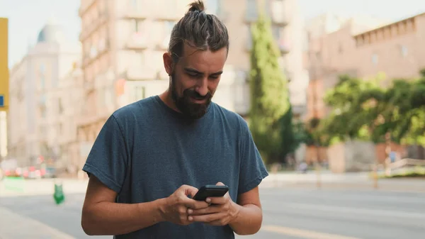 Young Smiling Man Beard Uses Cellphone Walks Street — Zdjęcie stockowe