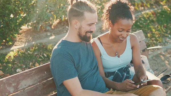 Happy Interracial Couple Talking While Sitting Bench Using Cellphone — Stock fotografie