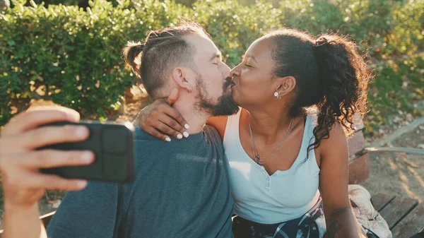 Happy Smiling Interracial Couple Kissing While Sitting Bench —  Fotos de Stock