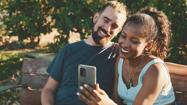 幸せな笑顔異人種間のカップル取ります自殺オン電話で座っている間公園のベンチ — ストック写真