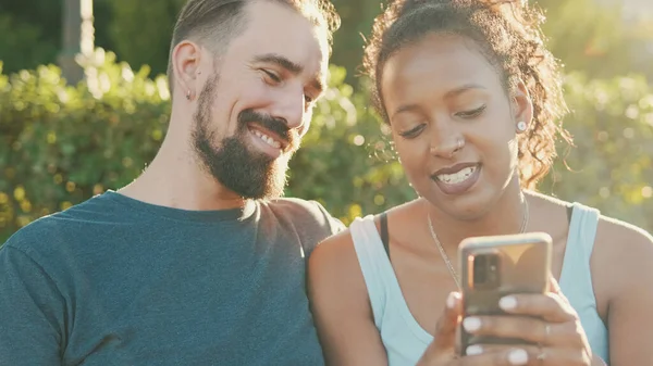 Happy Interracial Couple Talking While Sitting Bench Using Cellphone — ストック写真