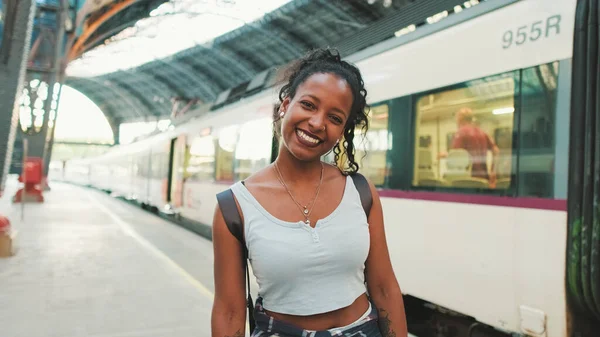 Close-up of smiling young mixed race woman standing at railway station on trains background