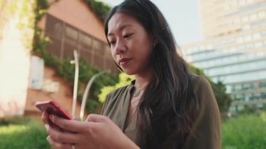 Genç kız modern binalarda otururken akıllı telefon kullanıyor.