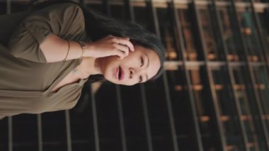 Genç iş kadını, iş merkezinin arka planında akıllı telefondan konuşuyor.