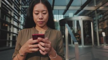 İş merkezinin arka planında dururken cep telefonu kullanan genç iş kadını