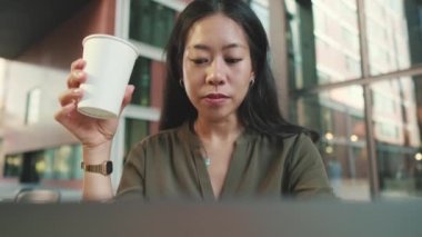 Dizüstü bilgisayarda çalışan ve kahve içen genç bir kadın.