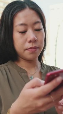 Yakın plan, genç kız modern binaların arka planında otururken akıllı telefon kullanıyor.