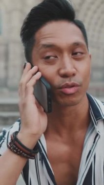 Merdivenlerde oturan ve arka planda manzaralı cep telefonuyla konuşan genç turistlerin yakın çekimi.