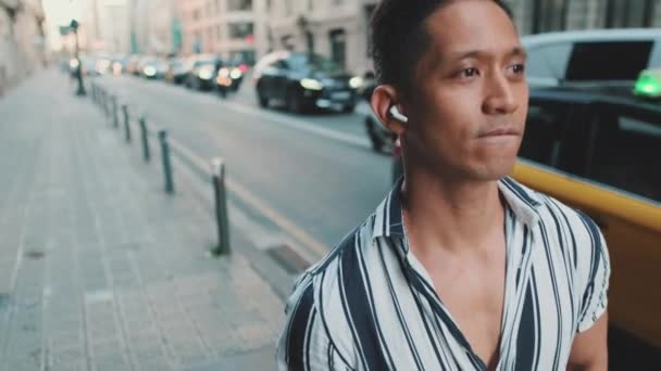若い男が道の横を歩いてヘッドフォンで音楽を聴く — ストック動画