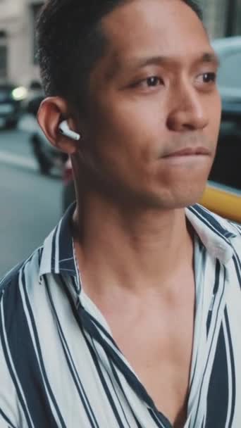 垂直ビデオ 若い男が道の隣を歩いてヘッドフォンで音楽を聴く — ストック動画