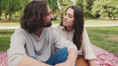 Mutlu, gülümseyen çift parkta battaniyede otururken konuşuyor.