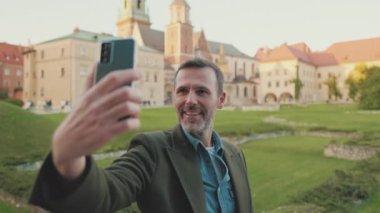 Adam eski şehrin arka planında cep telefonundan selfie çekiyor.