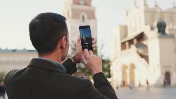 男は旧市街の広場に立って写真を撮る バックビュー — ストック動画