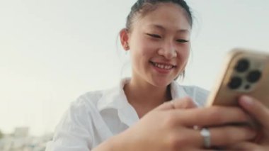 Deniz manzarası arka planında cep telefonu kullanan gülümseyen genç bir kadın.