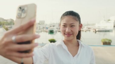 Deniz manzaralı cep telefonuyla selfie çeken genç bir kadın.