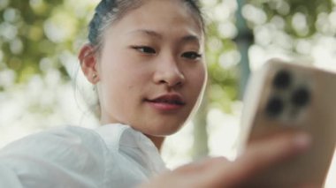 Bankta oturan ve cep telefonu kullanan genç bir kadının yakın çekimi.