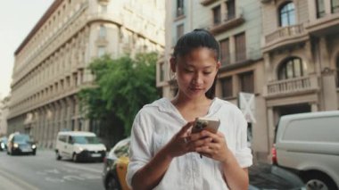 Yolun kenarında dururken cep telefonu kullanan gülümseyen genç bir kadın.