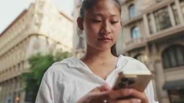 Kapatın, genç gülümseyen kadın yolun kenarında dururken cep telefonu kullanıyor.