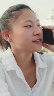 Deniz manzarası arka planında cep telefonu kullanan gülümseyen genç bir kadın.