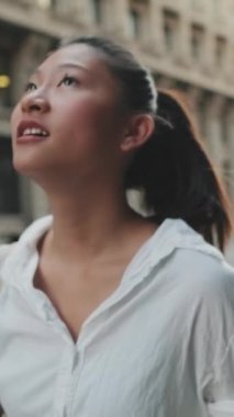 Genç bir kadın caddede yürür ve etrafa bakar.